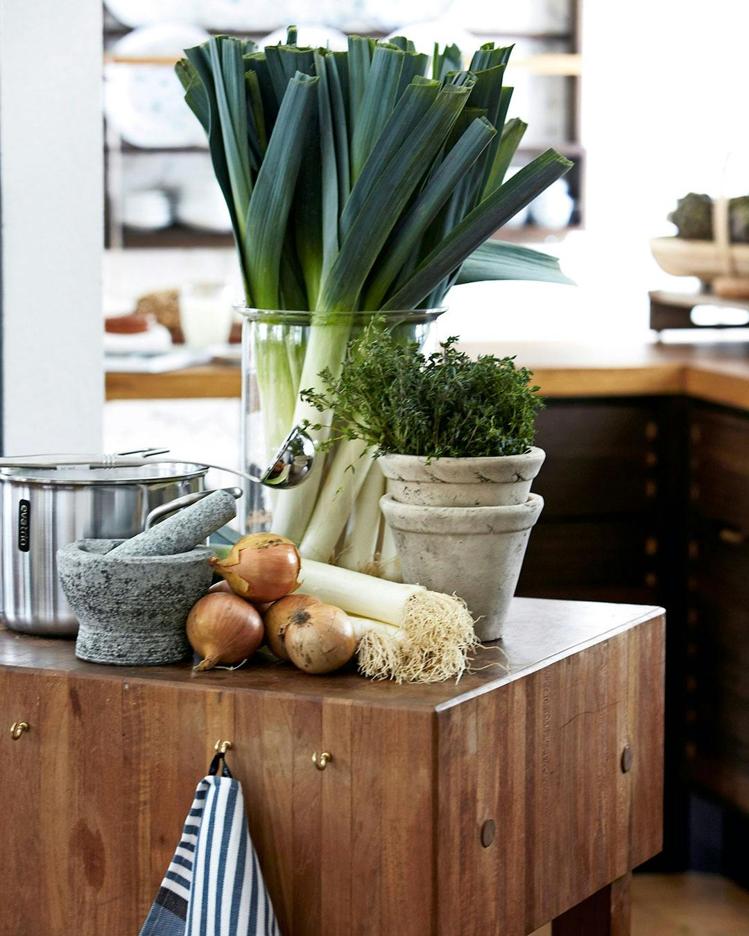 Porrer, løg og morter på køkkenbord.