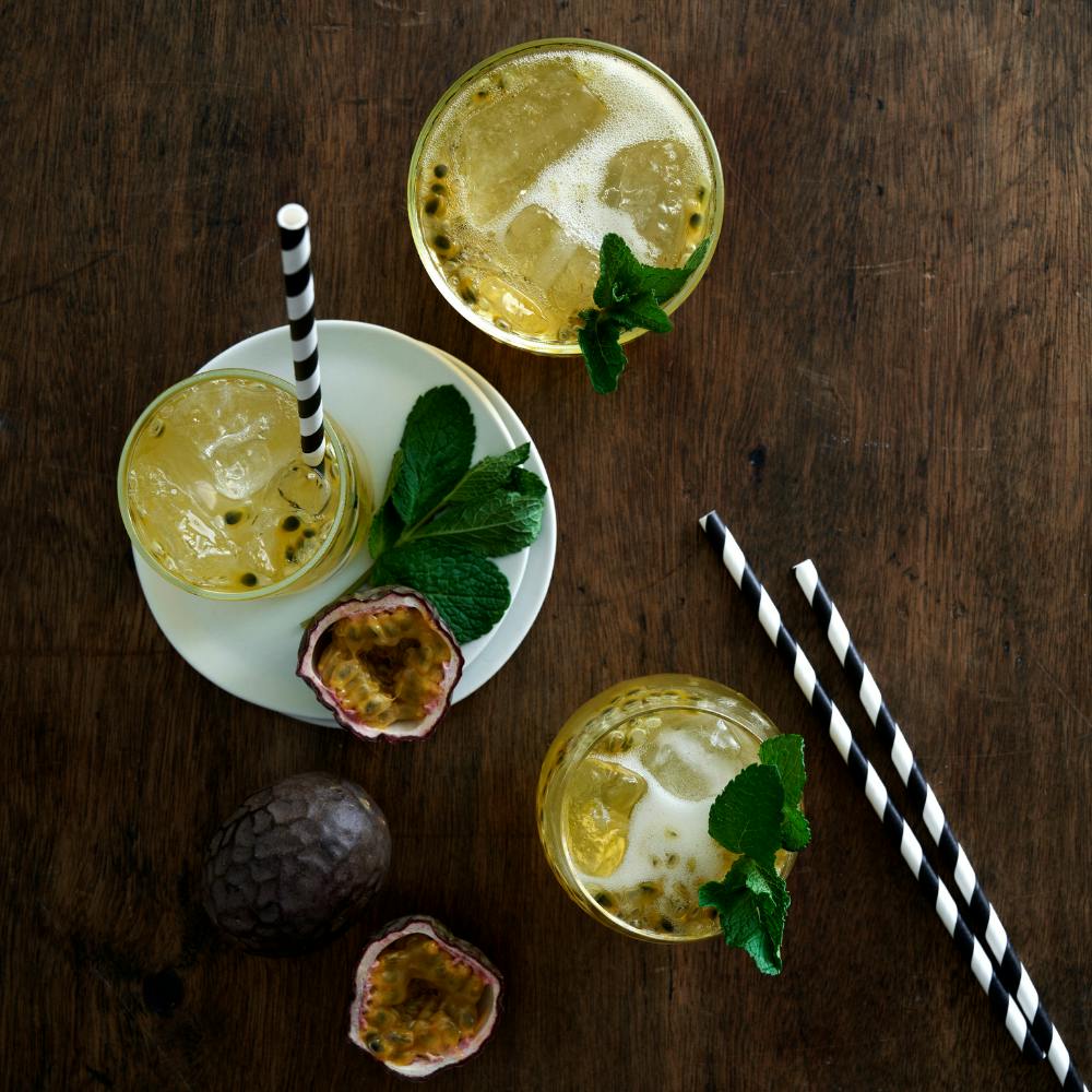 drink med champagne og passionsfrugt med hele mynteblade og stribede sugerør på et mørkbejdset træbord