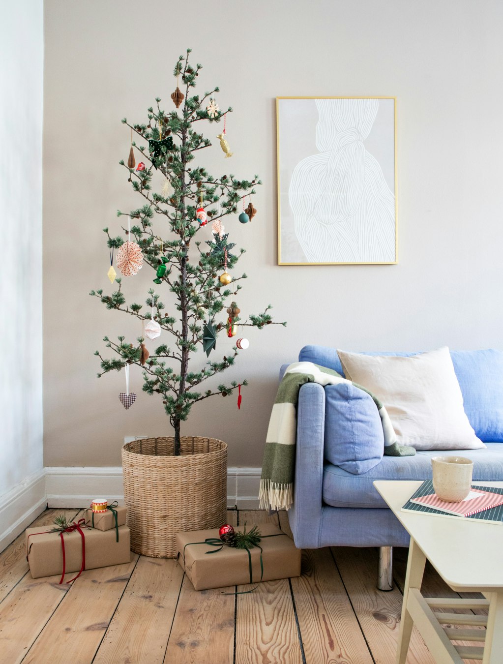 Cedertræ pyntet op til jul med ornamenter og gaver omkring ved siden af lyseblå sofa