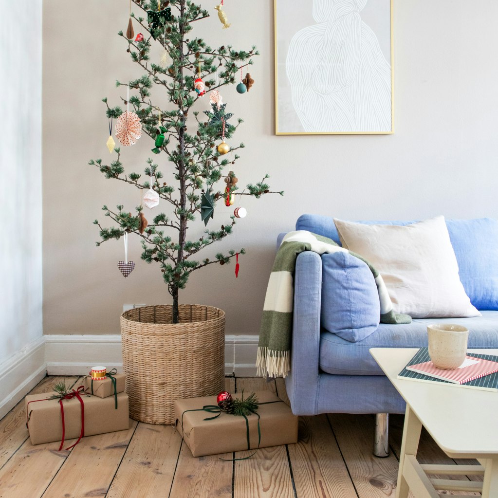 Cedertræ pyntet op til jul med ornamenter og gaver omkring ved siden af lyseblå sofa