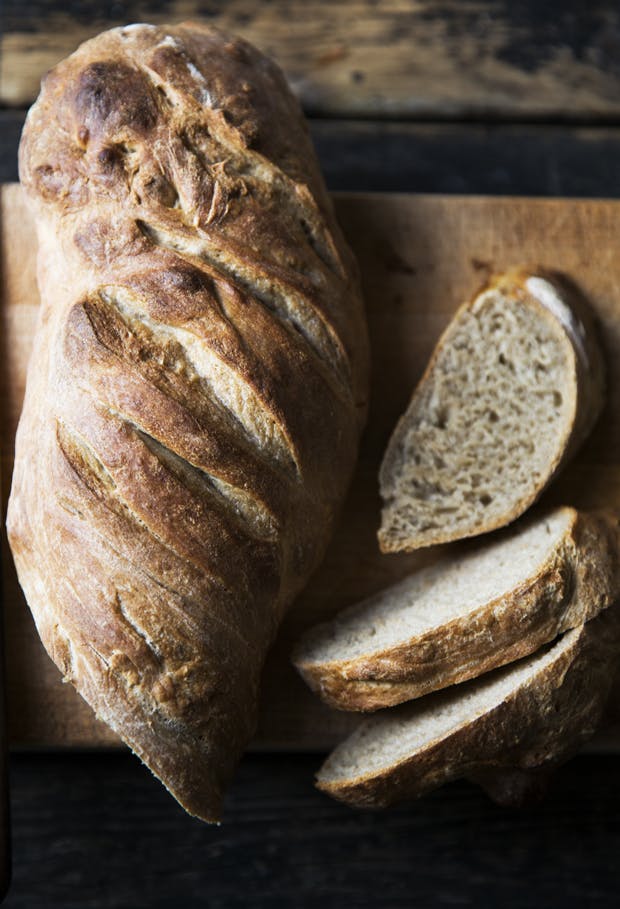 Friskbagt brød med en sprød skorpe og et par friskskårede skiver ved siden af.
