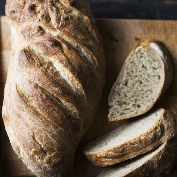 Friskbagt brød med en sprød skorpe og et par friskskårede skiver ved siden af.