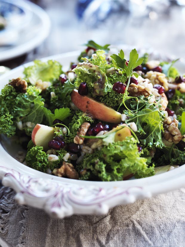 Grov salat med grønkål, nødder og æbler anrettet i en hvid skål.