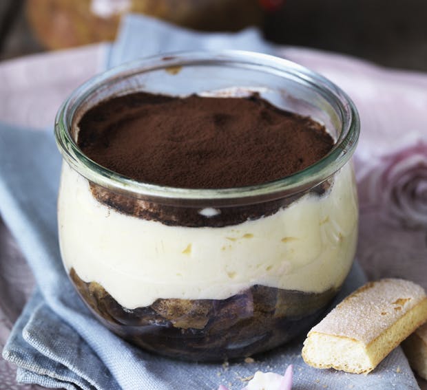 Tiramisu med ladyfingers nederst, et tykt lag mascarponecreme ovenpå og drys af kakao øverst. Anrettet i portionsglas.