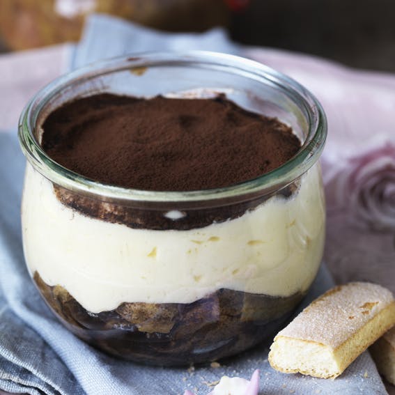 Tiramisu med ladyfingers nederst, et tykt lag mascarponecreme ovenpå og drys af kakao øverst. Anrettet i portionsglas.