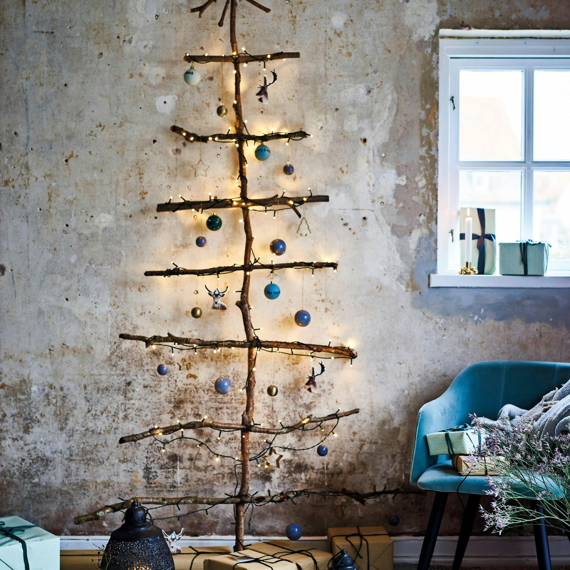 Vægjuletræ af grene med lys og julepynt